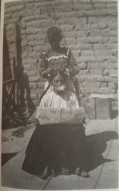 an old black and white photo of a woman sitting in front of a brick wall