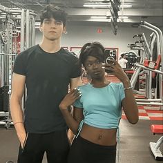 a man and woman standing next to each other in a gym holding up cell phones