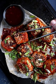 someone holding chopsticks over some food on top of a paper plate with sauce