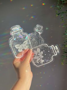 a hand holding an object in the shape of a bottle with butterflies and flowers on it