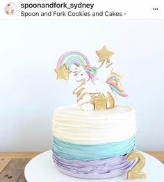 a white cake topped with a rainbow unicorn on top of a wooden table