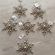 six snowflakes with tags attached to them sitting on a marble surface, one is white and the other is silver