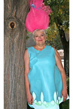 an older woman wearing a blue dress and pink hat standing next to a large tree