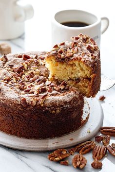 there is a cake with pecans on the plate next to it and a cup of coffee