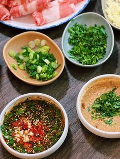 several bowls with different types of food in them on a wooden table next to meat and vegetables