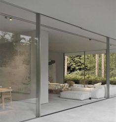 an open living room with glass walls and white furniture in the center, surrounded by greenery