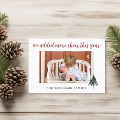 a christmas card with an image of a baby in a crib and pine cones