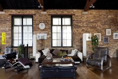 a living room filled with lots of furniture next to tall windows and wooden floors in front of a brick wall