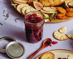 a plate with crackers and jam on it next to a jar of fruit preserves