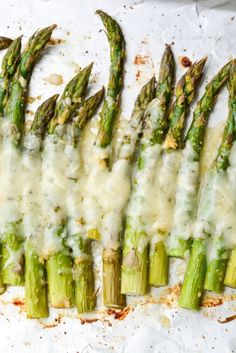 asparagus covered in melted cheese on top of a sheet of parchmented paper