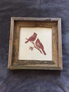 two red birds are sitting on a branch in a wooden frame with a black background