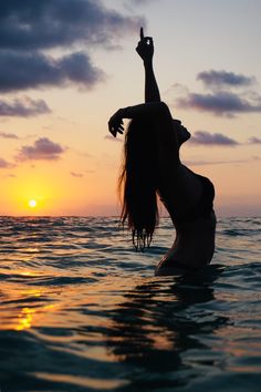 a woman standing in the ocean at sunset with her arms up and legs spread out