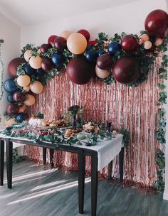 a table topped with lots of balloons next to a wall covered in foil streamers