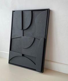 an art piece sitting on top of a white floor next to a black frame with abstract shapes