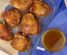 a glass dish filled with cooked chicken next to a cup of tea on a blue napkin