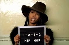 a woman wearing a hat holding up a sign that says hip hop on the front