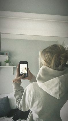 a woman taking a selfie in front of a mirror with her cell phone while sitting on a bed