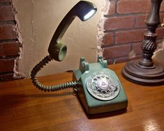 an old - fashioned telephone sits on a wooden table next to a lamp and brick wall