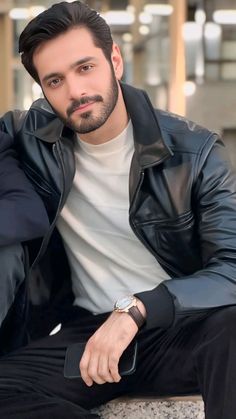 a man sitting on top of a cement wall wearing a black jacket and white t - shirt