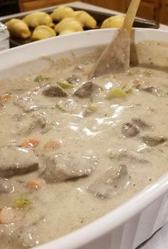 a white bowl filled with soup next to some potatoes and other food on a table