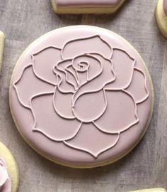 decorated cookies with frosting and icing on a sheet of paper next to pink roses