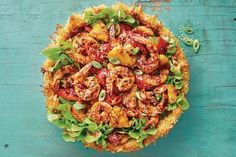 an overhead view of a pizza topped with shrimp and lettuce on a blue surface