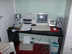 a desk with a computer, keyboard and speakers on it in front of a door