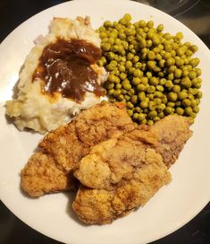 a white plate topped with chicken, mashed potatoes and gravy next to peas