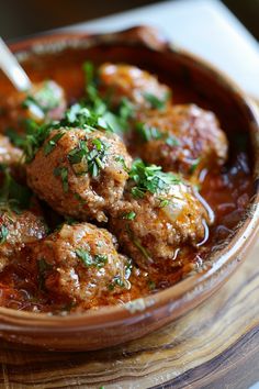 a wooden bowl filled with meatballs covered in sauce and garnished with parsley