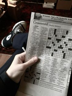 a person is holding up a crossword puzzle book in their hand while sitting on the floor