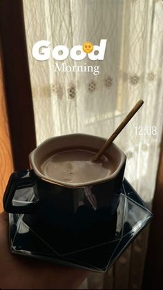 a cup of chocolate with a spoon in it sitting on a plate next to a window