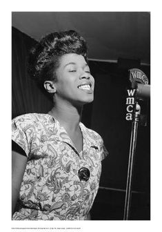 a black and white photo of a woman in front of a microphone smiling at the camera