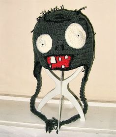 a crocheted black hat with white eyes and long hair on top of a pair of scissors