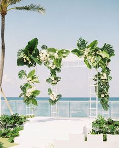 an outdoor wedding ceremony setup with white chairs and greenery on the aisle, overlooking the ocean