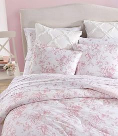 a bed with pink and white comforters in a bedroom next to a nightstand on a wooden floor