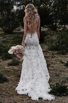 a woman in a white wedding dress standing on the grass with her back to the camera