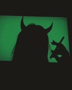 the silhouette of a woman with horns on her head holding a knife in front of a green screen