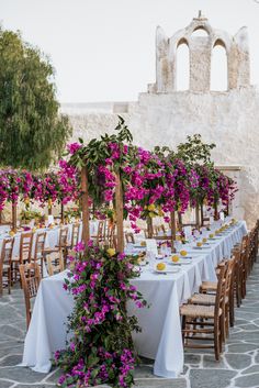 an outdoor dining area with tables and chairs covered in white tablecloths, purple flowers on each table