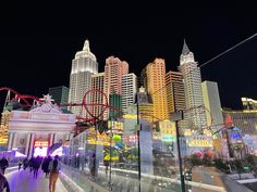 people are walking on the walkway in front of some tall buildings at night with colorful lights