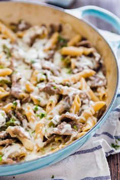 a blue casserole dish filled with pasta and meat covered in white sauce on a wooden table