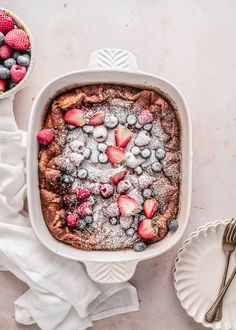 a baked dish with berries and powdered sugar on top, next to other dishes