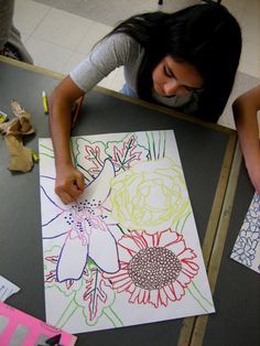 a woman is drawing flowers on paper with colored pencils