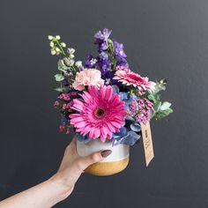 a person holding a flower pot with pink and purple flowers in it on a table