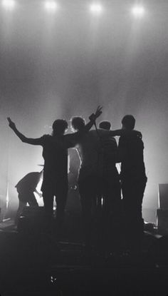 black and white photo of people on stage with their arms in the air while one person holds his hand up