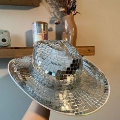 a person's hand holding up a silver disco ball hat on top of a mirror plate