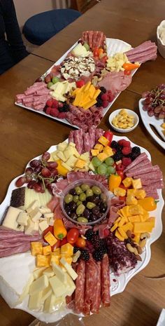 a table topped with plates filled with different types of cheeses and meats next to bowls of fruit