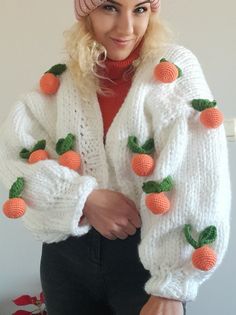 a woman with blonde hair wearing a white knitted sweater and orange fruit decorations on the sleeves