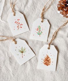 three tags with watercolor designs are hanging from twine on a white tablecloth