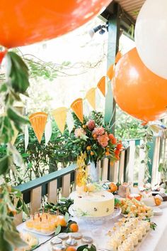 an outdoor party with orange and white balloons, cake and desserts on the table