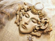 a close up of a face on top of a cloth covered bed with an ornate head piece